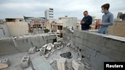 People stand next to a damaged roof after a rocket attack on U.S.-led forces in and near Irbil International Airport in Irbil, Iraq, Feb. 16, 2021.