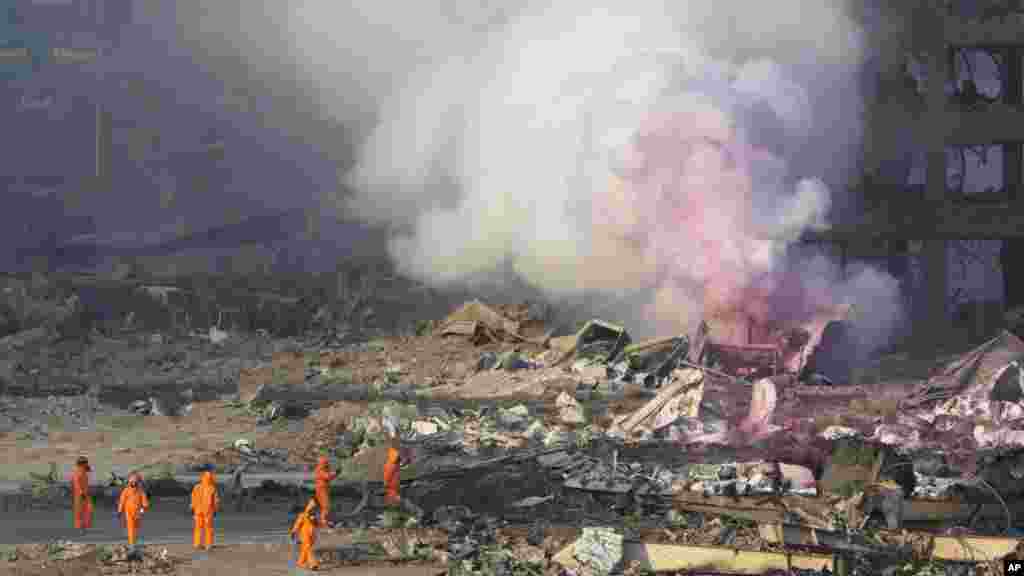 Para petugas pemadam kebakaran bersiaga saat asap merah muda membubung ke langit menyusul ledakan di sebuah gudang di Tianjin, China (13/8). ​(AP/Ng Han Guan)