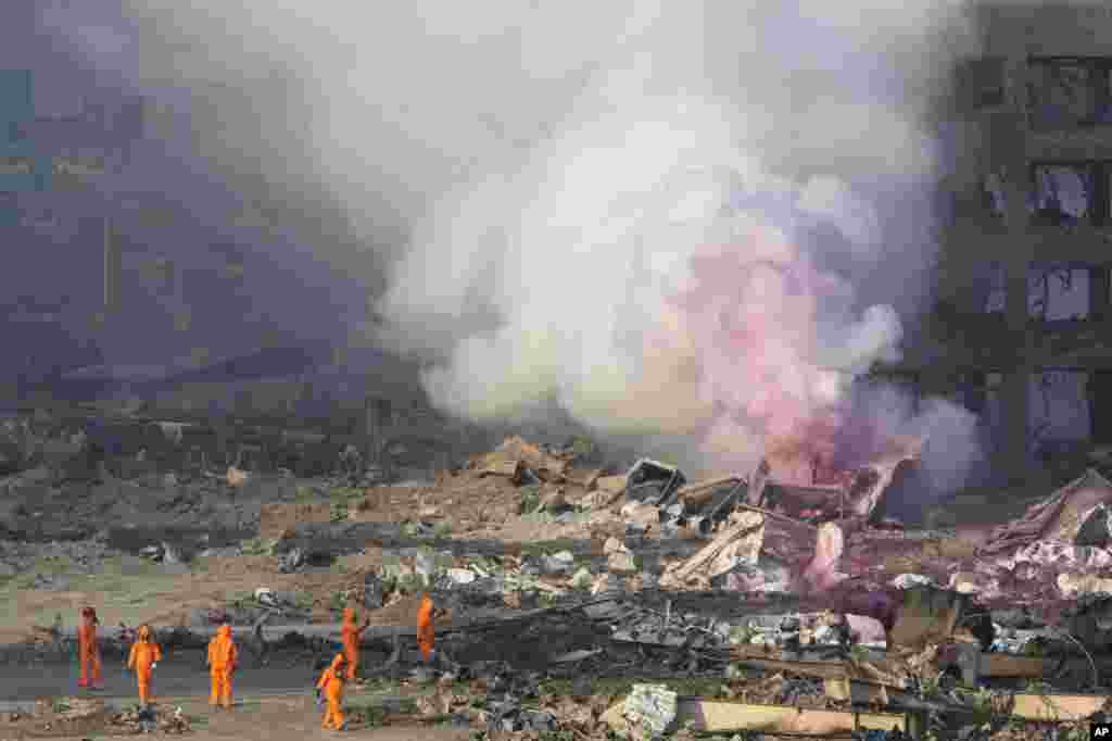 Firefighters in protective gear stand by as pink smoke billows up into the sky after an explosion at a warehouse in northeastern China&#39;s Tianjin municipality, Aug. 13, 2015.