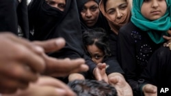 FILE - Mosul residents reach out for freshly baked cookies at a food distribution point inside western Mosul, Iraq, May 2, 2017. As Iraqi forces continue to make slow progress in the fight against the Islamic State group in Mosul, food supplies are running dangerously low for civilians trapped inside militant-held territory and those inside recently retaken neighborhoods.