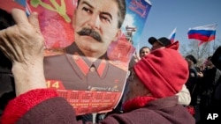 An elderly woman holds a calendar depicting Soviet leader Josef Stalin while watching a broadcast of Russian President Vladimir Putin's speech on Crimea in Sevastopol, Crimea, Tuesday, March 18, 2014.