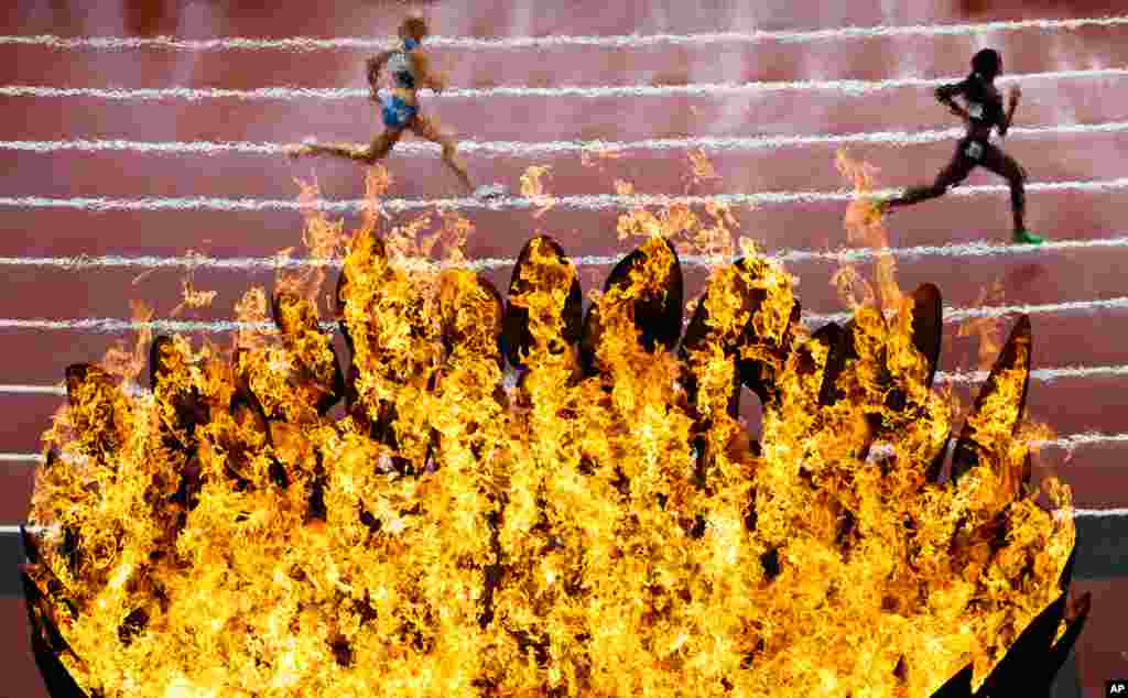 August 3: Runners pass by the Olympics flame on the first day of the athletics in the Olympic Stadium at the 2012 Summer Olympics in London.