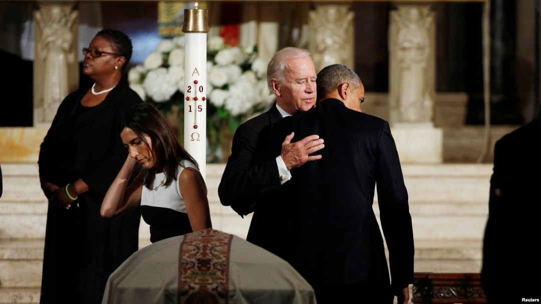President Barack Obama, back to camera, hugs Vice President Joe Biden during the funeral of his son former Delaware Attorney General Beau Biden as Biden's widow Hallie, left, passes her husband's casket at St. Anthony of Padua church in Wilimington, Del.,