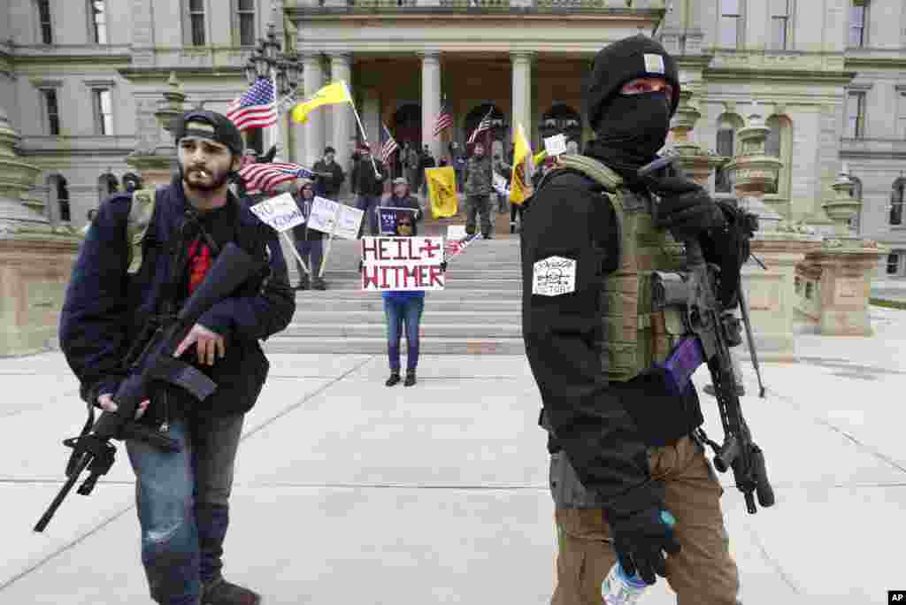 Protesters carry guns near the steps of the Michigan State Capitol building in Lansing, Michigan, April 15, 2020. Flag-waving, loud protesters drove past the Michigan Capitol to show their displeasure with Governor Gretchen Whitmer&#39;s orders to keep people at home and businesses closed during the coronavirus outbreak.