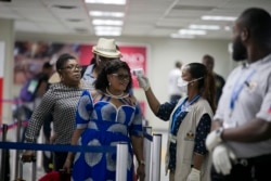 A Public Health Ministry nurse measures the temperature of a passenger arriving from France, at the Toussaint Louverture International Airport in Port-au-Prince, Haiti, Feb. 4, 2020.