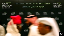 FILE - Participants walk in front of a banner for the Future Investment Initiative conference, in Riyadh, Saudi Arabia, Oct. 24, 2018.