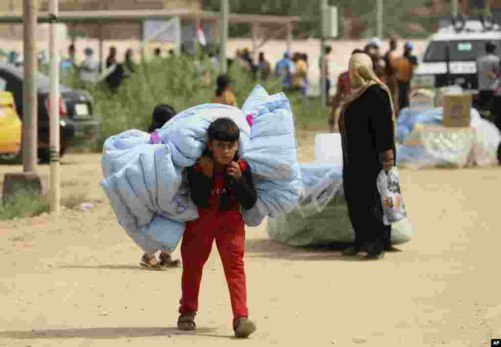 이라크 바그다드 서부 가잘리야의 난민촌에서 피난민 어린이가 구호품으로 받은 이불을 매고 있다.