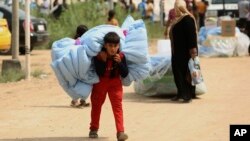 FILE - Internally displaced Iraqis carry humanitarian aid being distributed at a refugee camp in Baghdad's western neighborhood of Ghazaliyah, Sept. 16, 2015. 