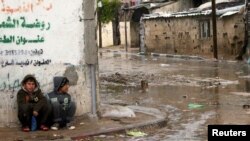 FILE - Palestinian boys sit on a sidewalk on a rainy day in Beit Hanoun in the northern Gaza Strip, Jan. 24, 2016. 