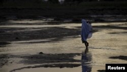 FILE - A woman walks across a river bed in Jalingo, Nigeria.