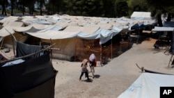 FILE - In this photo taken on Tuesday, July 14, 2016, two young girls walk among tents at Ritsona refugee camp north of Athens.