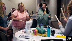 Teachers and guidance counselors tap wooden sticks during a rhythm exercise during a workshop helping teachers find a balance in their curriculum while coping with stress and burnout in the classroom on August 2, 2022 in Concord, New Hampshire. (AP Photo/Charles Krupa)