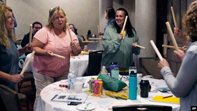 Teachers and guidance counselors tap wooden sticks during a rhythm exercise during a workshop helping teachers find a balance in their curriculum while coping with stress and burnout in the classroom on August 2, 2022 in Concord, New Hampshire. (AP Photo/Charles Krupa)