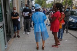 A medical technician wearing a face shield talks to a masked woman who waits to get tested for COVID-19 outside a laboratory in Paris, Aug 8, 2020.