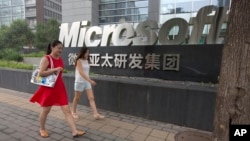 FILE - women walk past the logo for Microsoft in Beijing, China, July 31, 2014.