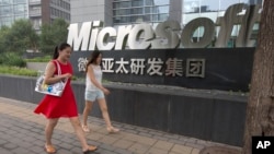 FILE - women walk past the logo for Microsoft in Beijing, China, July 31, 2014.
