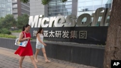 FILE - Women walk past the logo for Microsoft in Beijing, China, July 31, 2014.