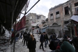 FILE - People walk past destruction by government airstrikes in the town of Ariha, in Idlib province, Syria, Jan. 15, 2020.