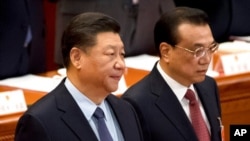 FILE - Chinese President Xi Jinping, left, stands as Premier Li Keqiang arrives for the closing session of China's National People's Congress at the Great Hall of the People in Beijing, March 15, 2019.