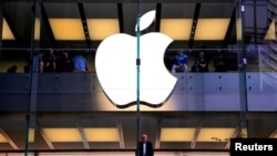 FILE PHOTO: A customer stands underneath an illuminated Apple logo as he looks out the window of the Apple store located in central Sydney