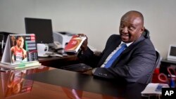 FILE - Athletics Kenya CEO Isaac Mwangi holds up a copy of the IAAF Competition Rules book, to illustrate his denial that Athletics Kenya would have the power to shave time off athletes’ bans, in Nairobi, Kenya, Feb. 8, 2016. 