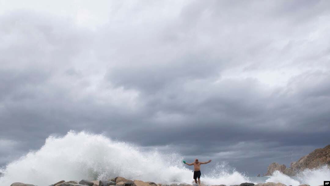 A tourist poses for a photo in front breaking waves before the expected arrival of Hurricane Lorena, in Los Cabos, Mexico, Friday, Sept. 20, 2019.