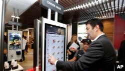 FILE - McDonald's CEO Steve Easterbrook demonstrates an order kiosk, with cashier Esmirna DeLeon, during a presentation at a McDonald's restaurant in New York's Tribeca neighborhood, Nov. 17, 2016.