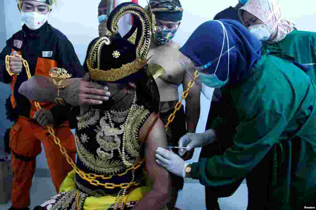 An Indonesian health care worker injects Sinovac&#39;s vaccine to a man dressed in Indonesia&#39;s traditional human puppet costume known as Wayang, as Indonesia drives mass vaccination for COVID-19, in Central Java province, Indonesia. (Antara Foto/via Reuters) 