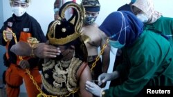 Seorang petugas kesehatan menyuntikkan vaksin Sinovac kepada seorang pria berkostum wayang, saat pemerintah melakukan vaksinasi massal untuk COVID-19, di Jawa Tengah. (Foto: Antara via Reuters)