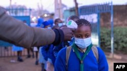 Les élèves de l'école primaire olympique font la queue pour faire mesurer leurs températures à l'entrée de l'école tôt le matin de la journée officielle de réouverture des écoles publiques le 4 janvier 2021, dans le bidonville de Kibera, au Kenya.