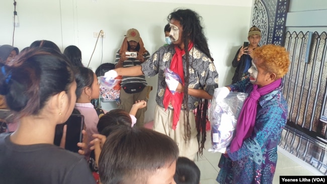 Dua pemain pantomim membagikan masker wajah untuk anak-anak di Posko Pengungsian Buah Hati, Kelurahan Karema, Kota Mamuju, Sulawesi Barat. Selasa (26/1/2021). (Foto: VOA/Yoanes Litha)