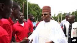 FILE- In this Thursday, Aug. 8, 2013 file photo, Borno state governor Kashim Shettima, right, shake hands with members of the "Civilian JTF", in Maiduguri Nigeria. The governor of Nigeria's northeast Borno state Shettima has temporarily relocated to the town of Bama, that was occupied by Boko Haram extremists for six months, in an effort to promote rebuilding.