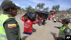 Policías colombianos observan el paso de colombianos deportados que cruzan el río Táchira en la frontera con Venezuela.