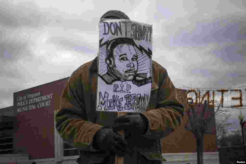 Um homem segura um cartaz com a cara de Michael Brown desenhada, apelando a acusação do polícia branco que atirou contra o jovem de 18 anos em Agosto último. O homem está à porta da esquadra da Polícia de Ferguson, Missouri. Nov. 24, 2014.