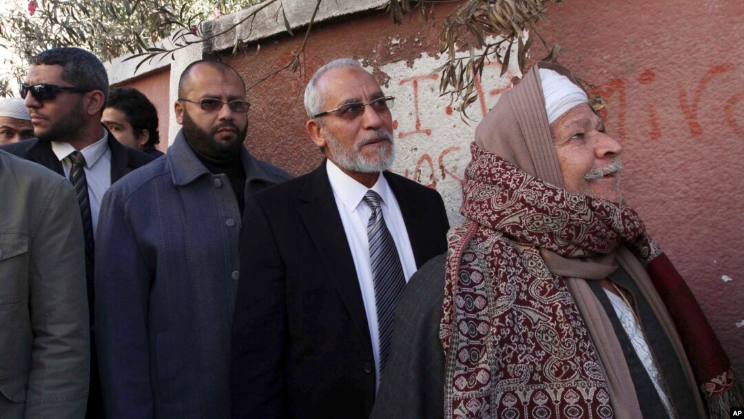 FILE - Muslim Brotherhood leader Mohammed Badie, second right, waits in line outside a polling place in Beni Suef, Egypt, to vote on a constitution drafted by Islamist supporters of President Mohammed Morsi. 
