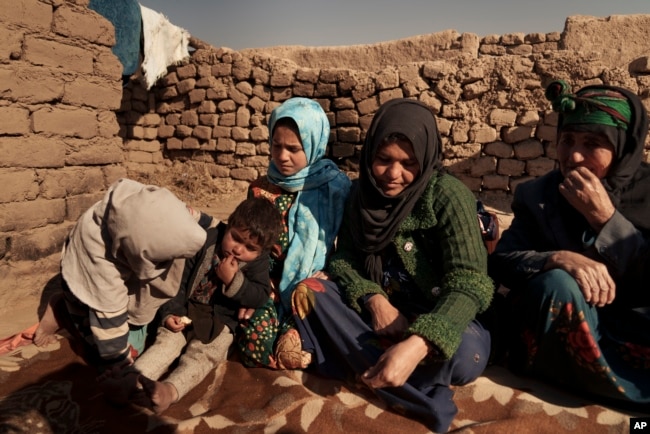 Aziz Gul, second from right, and her 10-year-old daughter Qandi, center, sit outside their home with other family members, near Herat, Afghanistan. Dec. 16, 2021. Qandi's father sold her into marriage without telling his wife, Aziz.