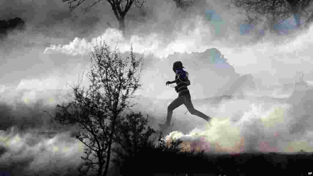 A Palestinian demonstrator runs through a cloud of tear gas during clashes against Israel's operations in Gaza Strip, outside Ofer, an Israeli military prison near the West Bank city of Ramallah, November 15, 2012.