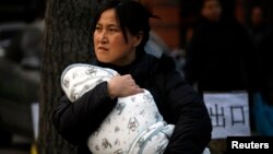 A mother carries her baby wrapped in a blanket in Beijing, (File photo).