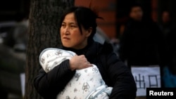 FILE - A mother carries her baby wrapped in a blanket in Beijing.