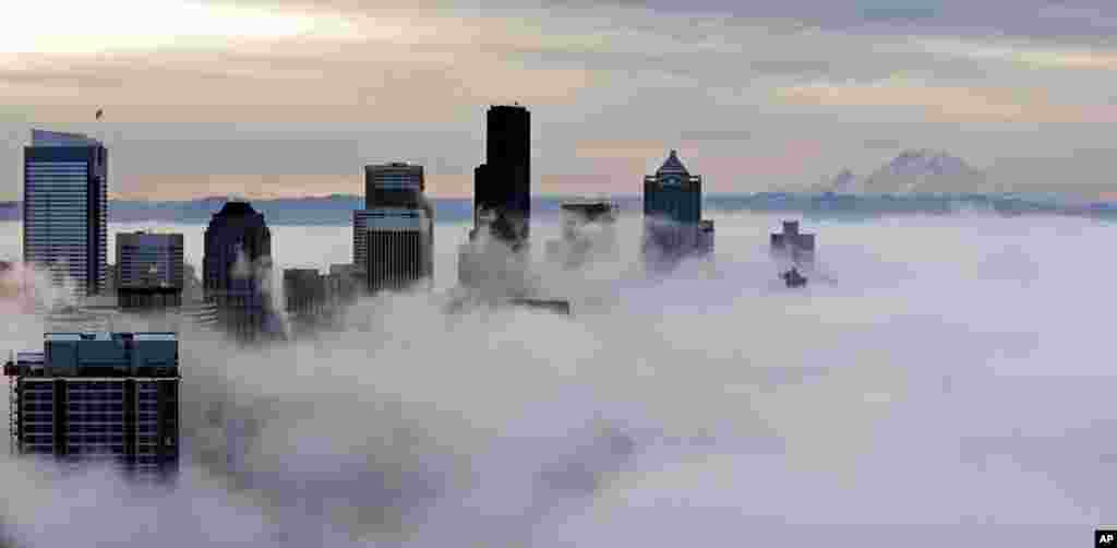 Downtown buildings rise above a low-level morning fog as Mount Rainier is seen some 130 kilometers in the distance, in this view from atop the Space Needle in Seattle, Washington, USA.