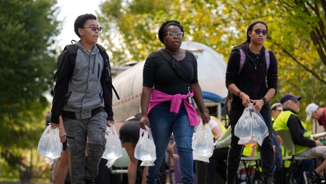 People carry bags of fresh water after filling up at a distribution site in the aftermath of Hurricane Helene, Oct. 2, 2024, in Asheville, NC.