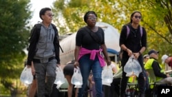 People carry bags of fresh water after filling up at a distribution site in the aftermath of Hurricane Helene, Oct. 2, 2024, in Asheville, NC.