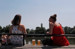 Two women sit with take away drinks from a pub on the banks of the river Thames in London, June 23, 2020.