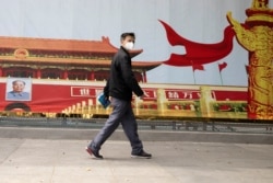 FILE - A resident wearing a mask against coronavirus walks past government propaganda poster featuring Tiananmen Gate in Wuhan in central China's Hubei province, Apr. 16, 2020.