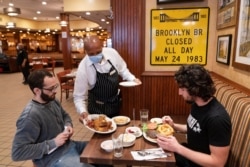 FILE - A waiter serves lunch to clients at Junior's Restaurant in New York. NYC will soon require proof of COVID-19 vaccinations for anyone who wants to dine inside at a restaurant.