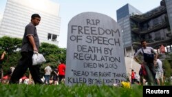 FILE - Protesters walk past a mock gravestone that reads "RIP Freedom of Speech" during a protest against new licensing regulations imposed by the government for online news sites, at Hong Lim Park in Singapore.