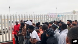 FILE - Migrants, many from Cameroon, listen to names being called for those who can claim asylum in the United States, in Tijuana, Mexico, July 28, 2019.