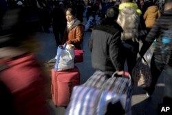 A woman with her luggage waits as Chinese passengers arrive at the Beijing railway station to catch trains in Beijing, Jan. 31, 2016.
