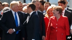 FILE - German Chancellor Angela Merkel, right, watches as U.S. President Donald Trump, left, shakes hands with French President Emmanuel Macron, center, during a ceremony at NATO headquarters in Brussels, May 25, 2017. 