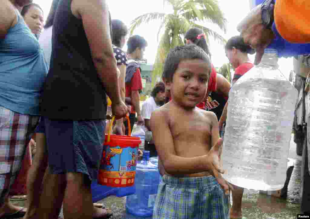 Seorang bocah laki-laki mengisi botol plastik dengan air setelah topan Haiyan menghantam kota Tacloban, Filipina tengah (11/11). (Reuters/Romeo Ranoco)